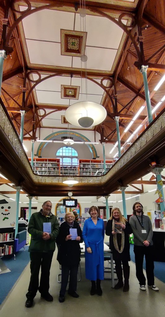 Angela Graham and four other people standing in Bargoed Library. The photo takes in the high wooden ceiling and balcony above them.